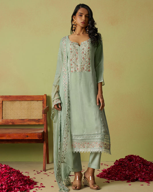 Woman wearing a light green traditional outfit with floral patterns against a green background.