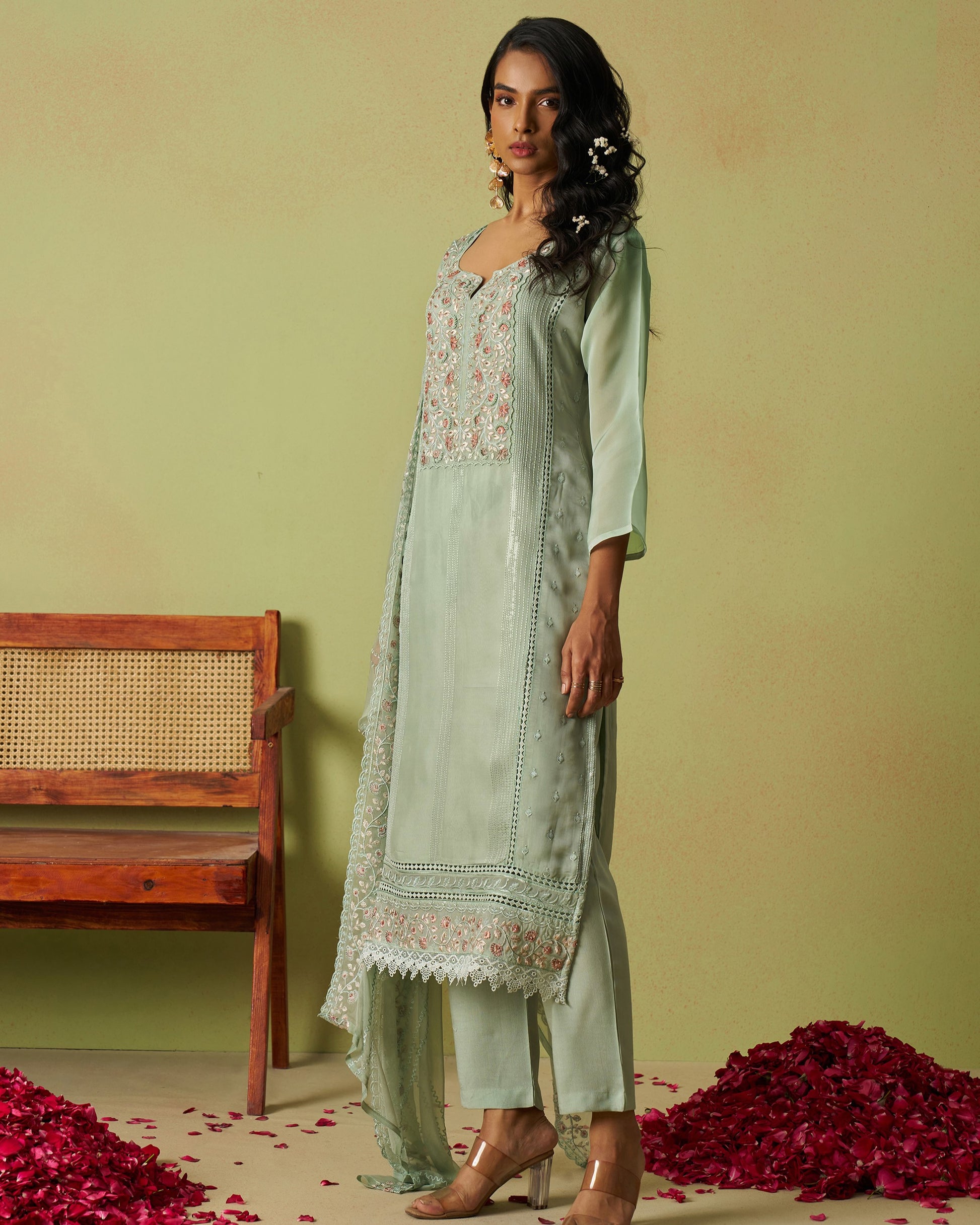 Woman in a light green traditional outfit with floral embroidery standing against a plain background.