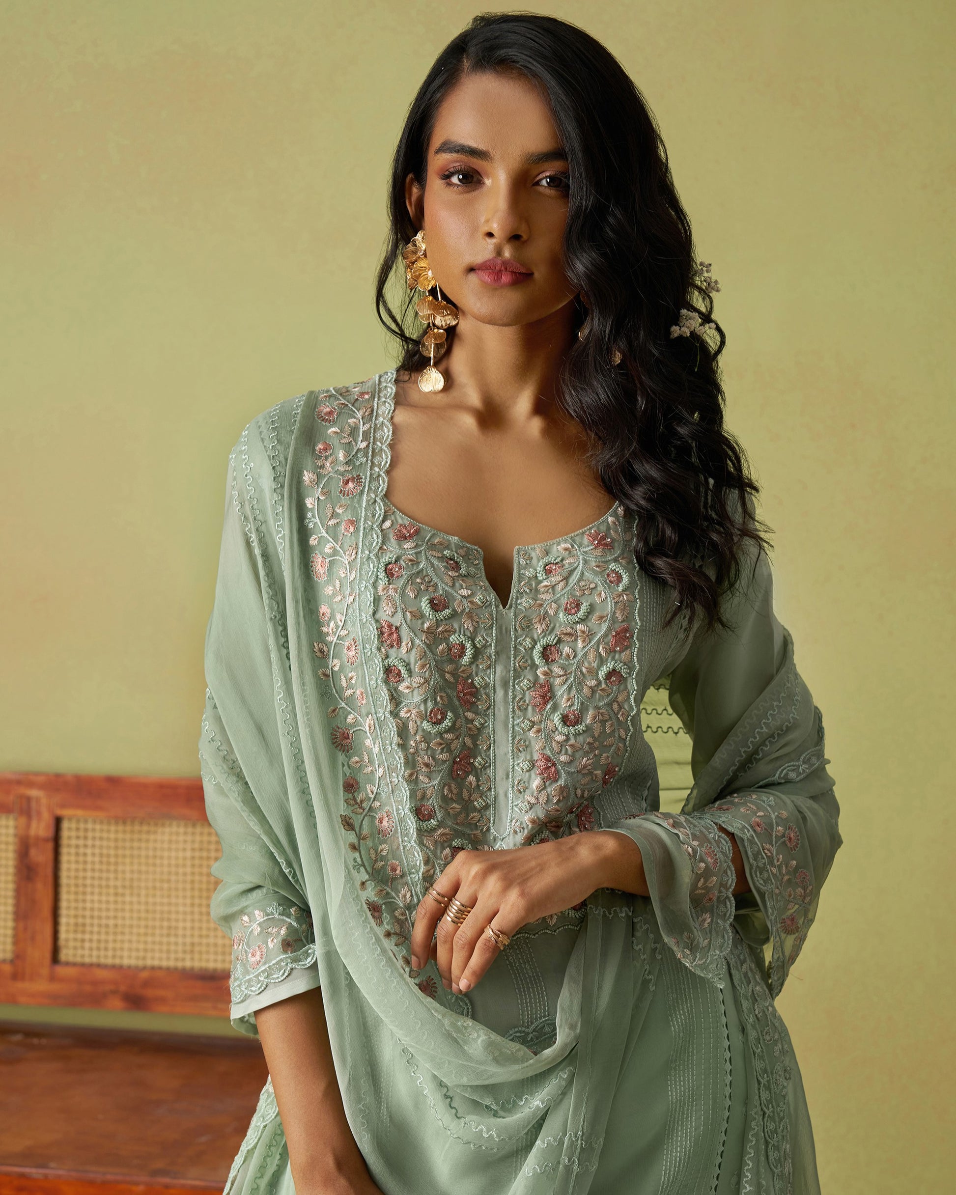 Woman wearing a light green traditional outfit with floral patterns against a beige background