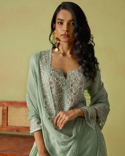 Woman wearing a light green traditional outfit with floral patterns against a beige background