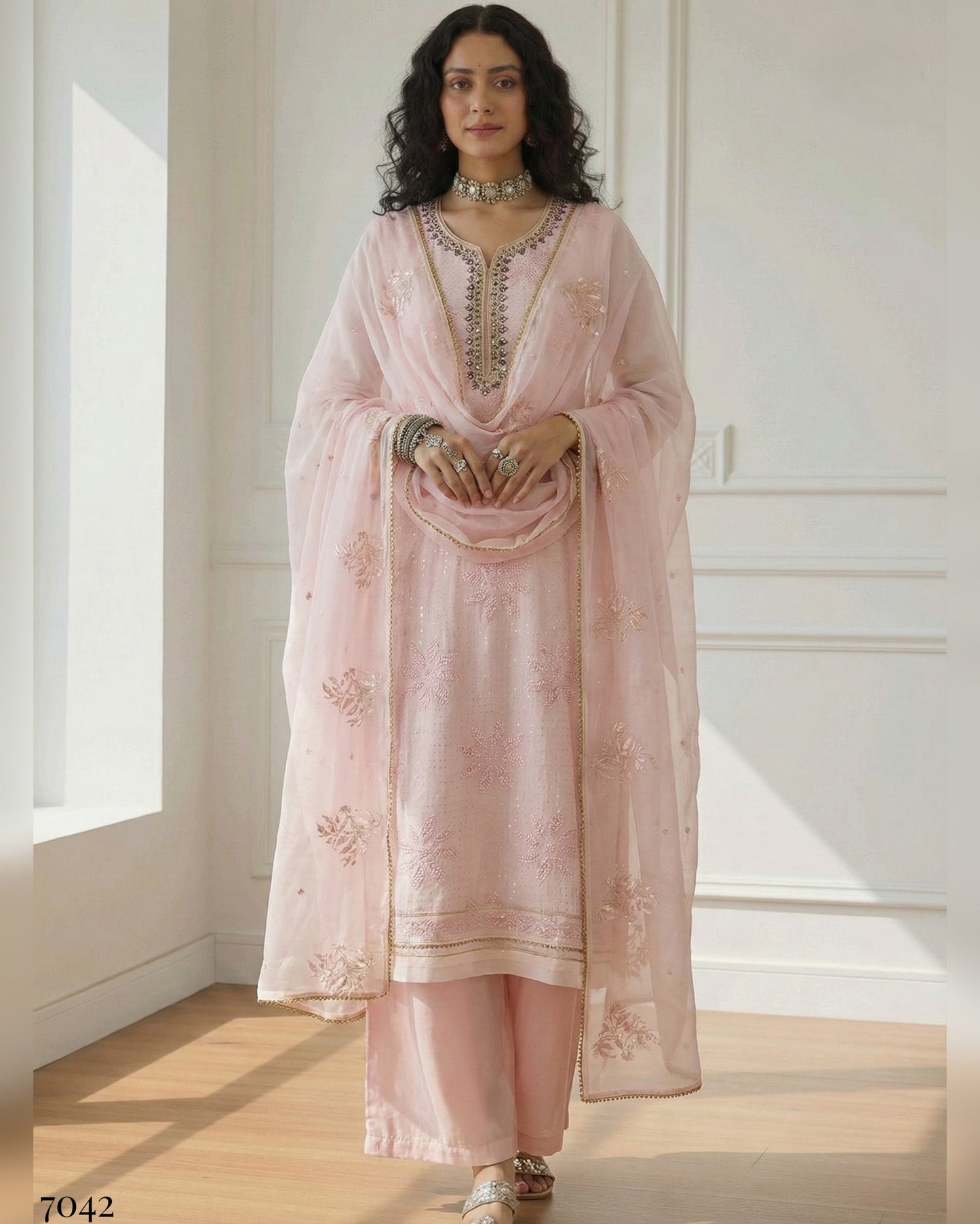 Woman wearing a light pink traditional outfit with embroidery in a bright room.