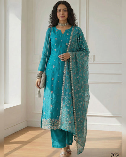 Woman wearing a teal traditional outfit with a matching dupatta in a bright room.