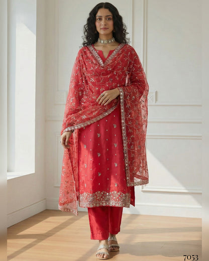Woman wearing a red traditional outfit with a matching dupatta in a bright room.