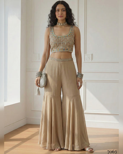 Woman wearing a beige outfit with a crop top and wide-leg pants in a well-lit room.