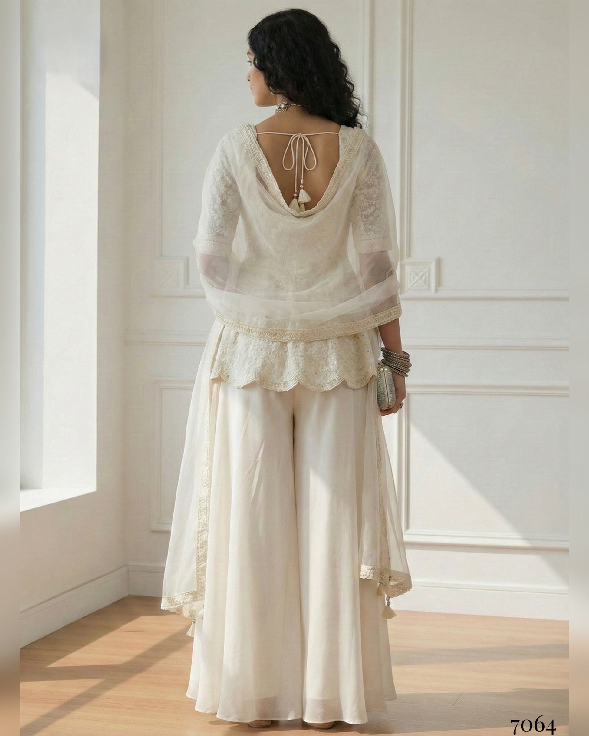 Woman wearing a white lace outfit standing in a bright room with sunlight streaming in.