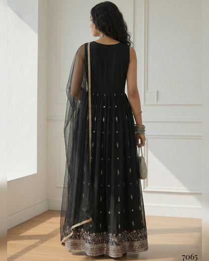 Woman wearing a black dress with sheer overlay in a bright room.