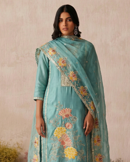 Woman wearing a light blue embroidered traditional outfit with a matching dupatta against a beige background