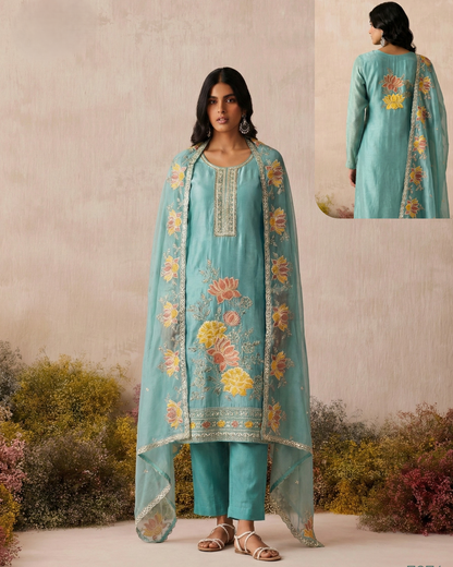 Woman wearing a turquoise embroidered outfit with floral patterns against a natural background