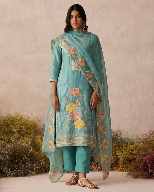 Woman wearing a turquoise embroidered outfit with a matching dupatta against a neutral background