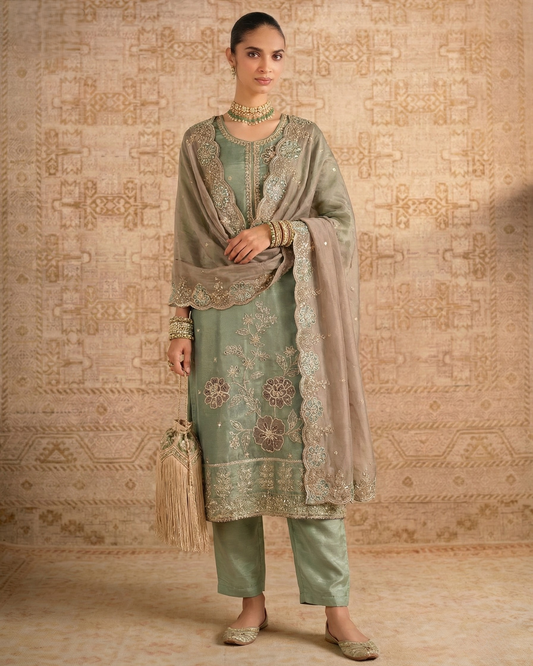 Woman in traditional outfit with embroidered shawl against a patterned wall