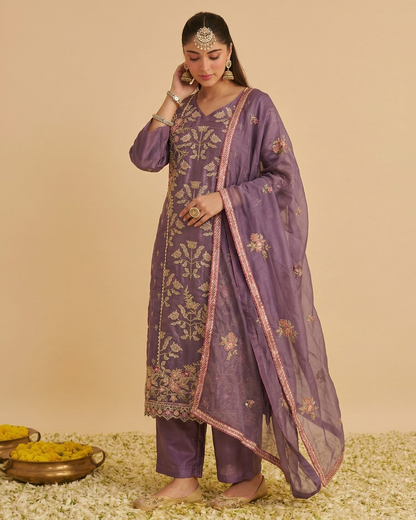 Woman wearing a purple embroidered traditional outfit on a beige background