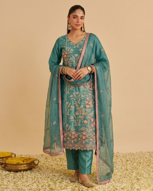 Woman wearing a teal embroidered outfit with a dupatta on a beige background