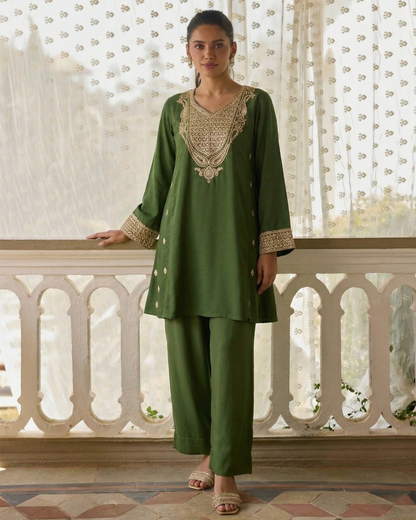 Woman wearing a green traditional outfit with intricate patterns in a decorative setting.