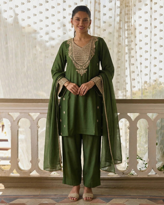 Woman wearing a green traditional outfit with intricate designs in a decorative setting.