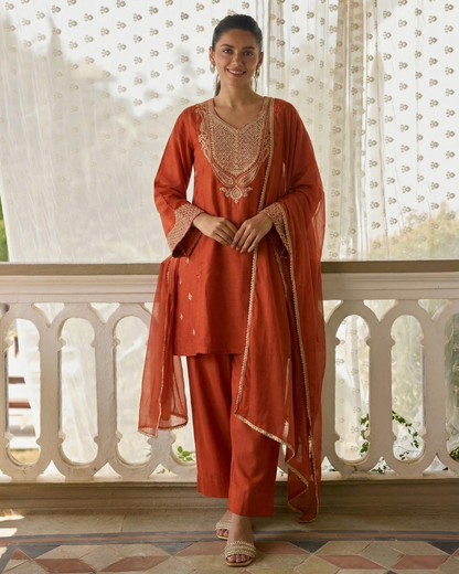 Woman in a traditional red outfit with intricate patterns standing on a balcony.