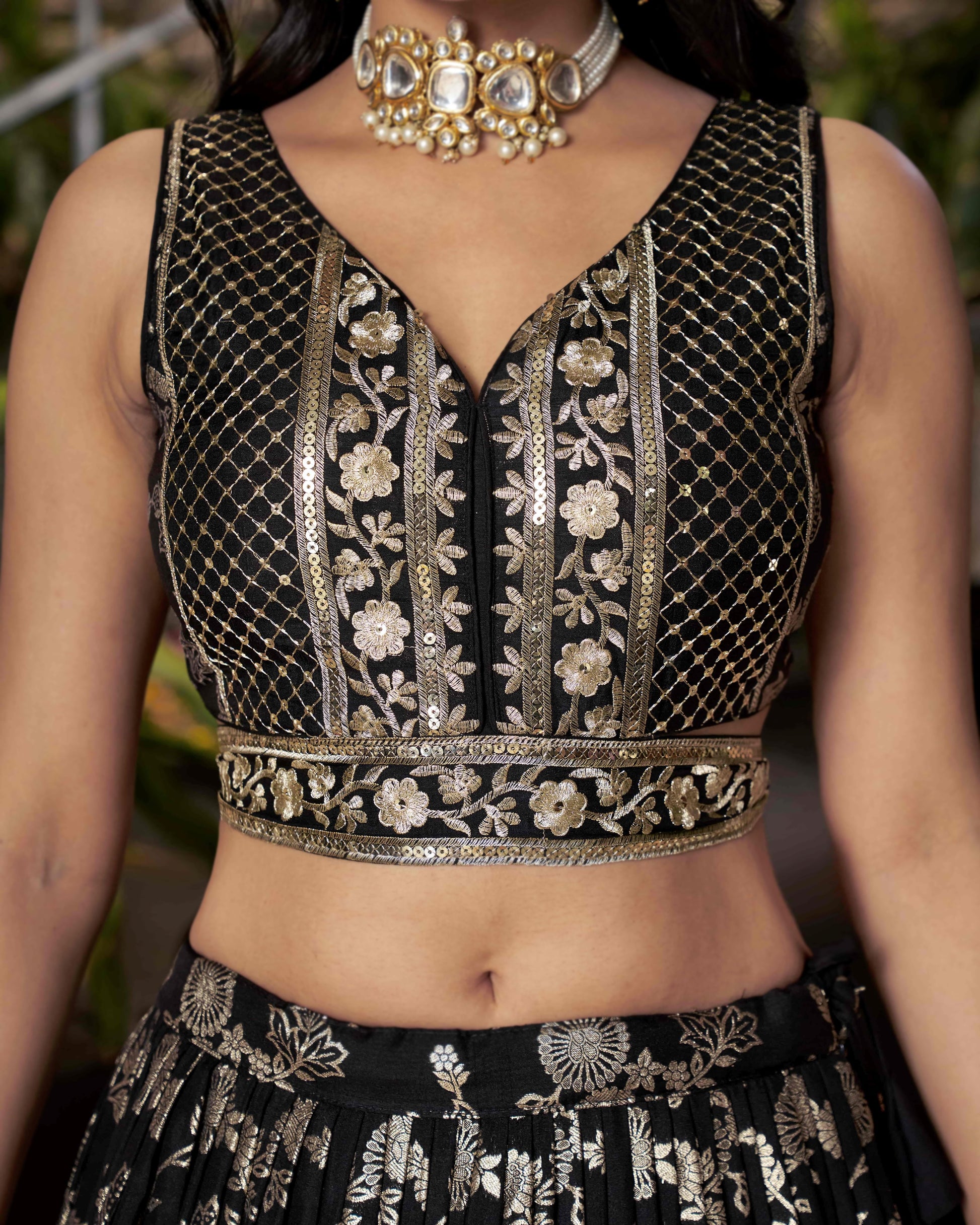Black embroidered top with gold details worn by a person, with a blurred background.