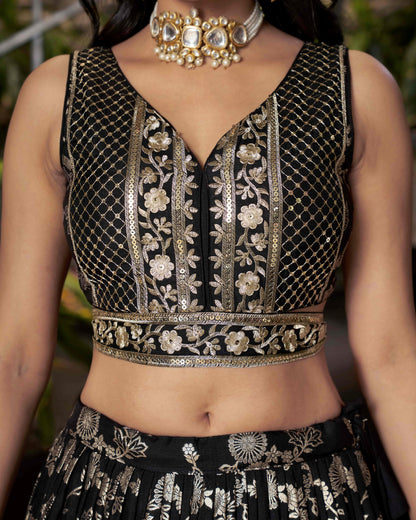 Black embroidered top with gold details worn by a person, with a blurred background.