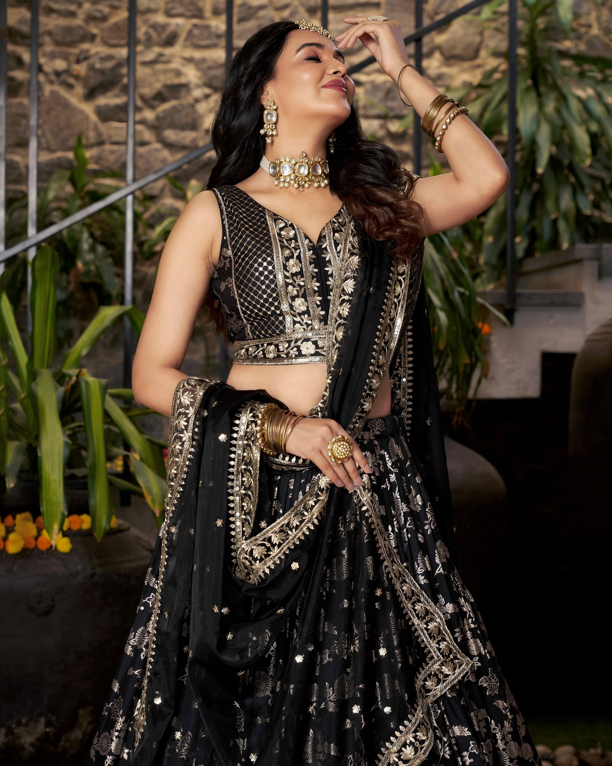 Woman in a black and gold traditional outfit with jewelry, standing outdoors.