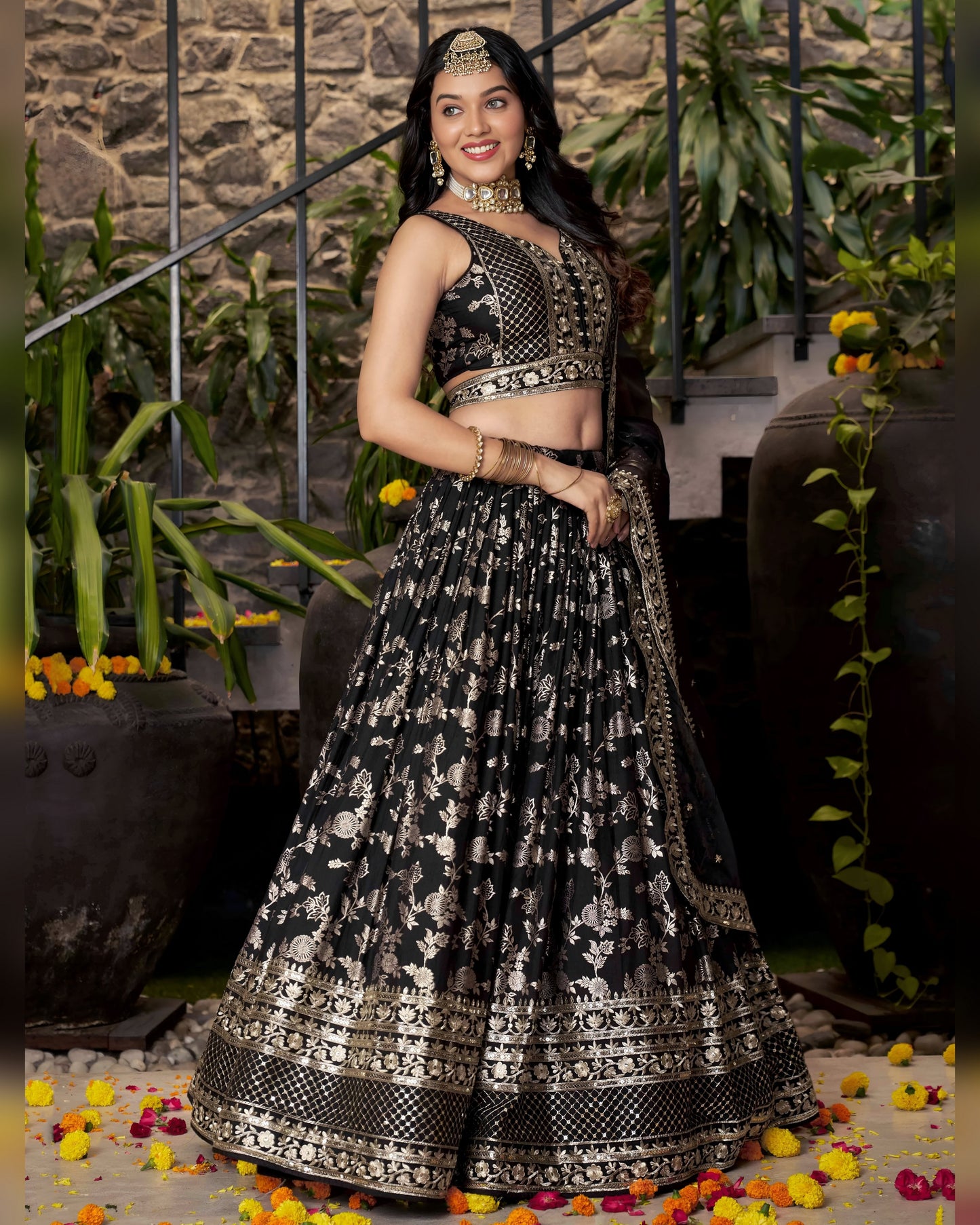 Woman in a black and white patterned traditional outfit standing in front of a stone wall with plants.