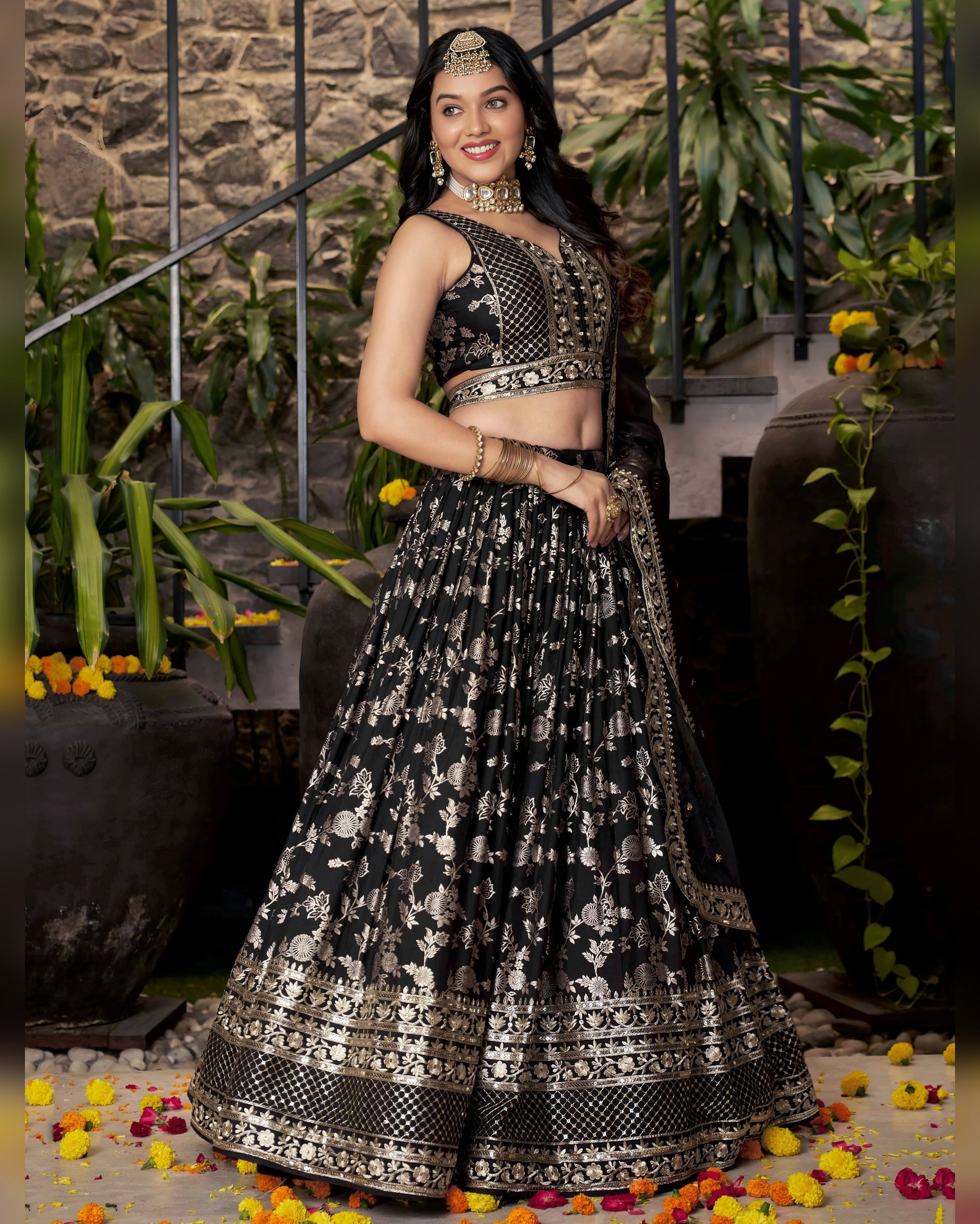 Woman in a black and white patterned traditional outfit standing in front of a stone wall with plants.