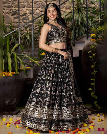 Woman in a black and white patterned traditional outfit standing in front of a stone wall with plants.