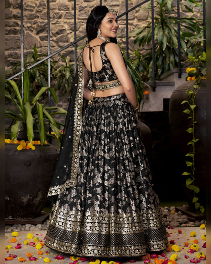 Woman in a black and white patterned traditional outfit standing in a decorative setting with flowers and plants.