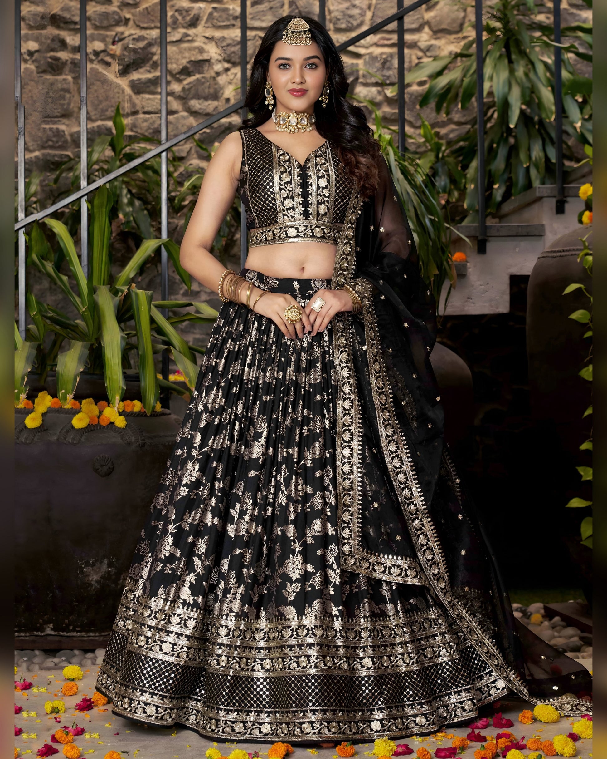Woman in a black and silver traditional outfit with a stone wall and plants in the background