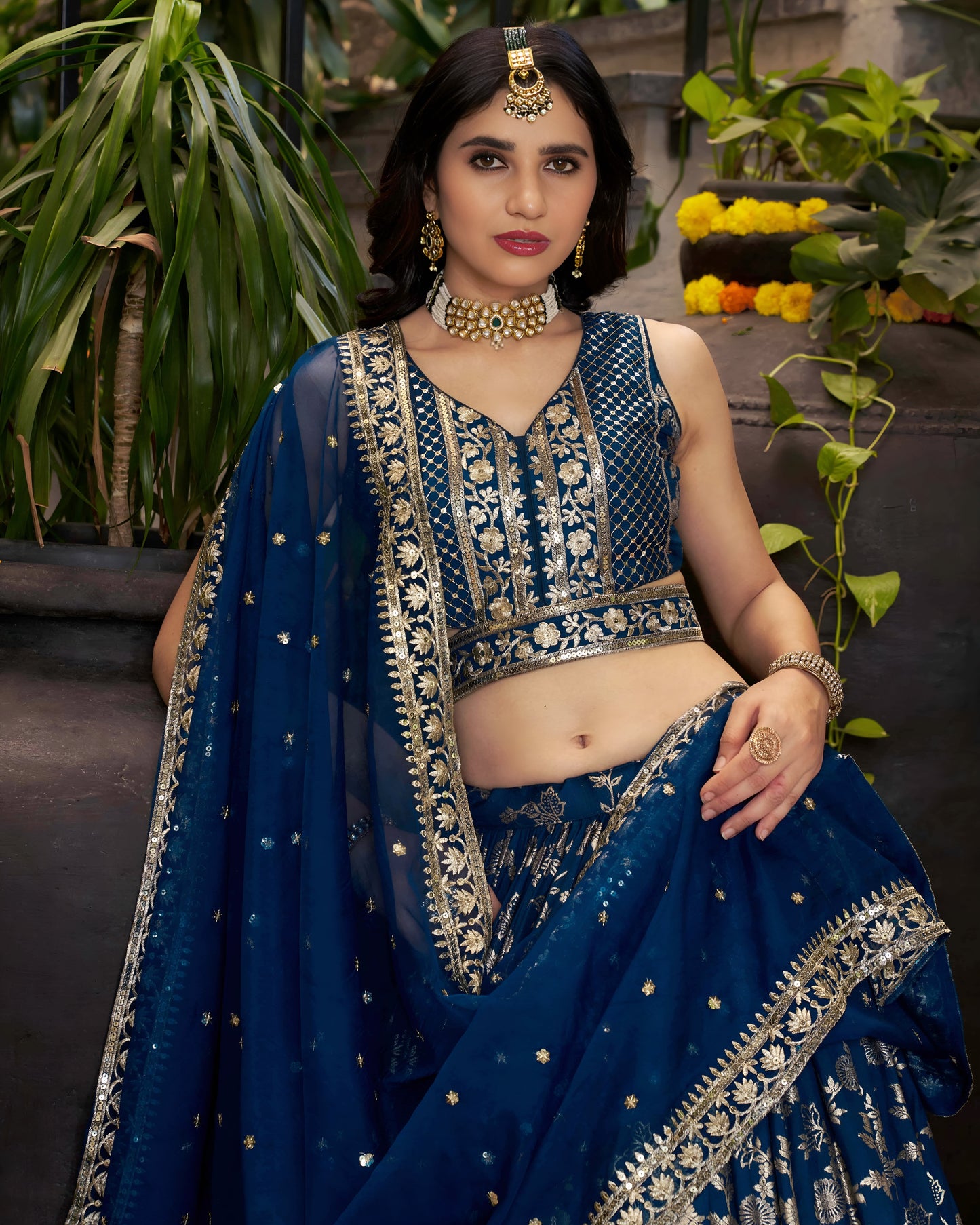 Woman in a blue embroidered traditional outfit with jewelry, standing outdoors.