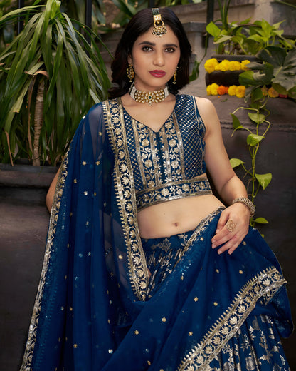 Woman in a blue embroidered traditional outfit with jewelry, standing outdoors.