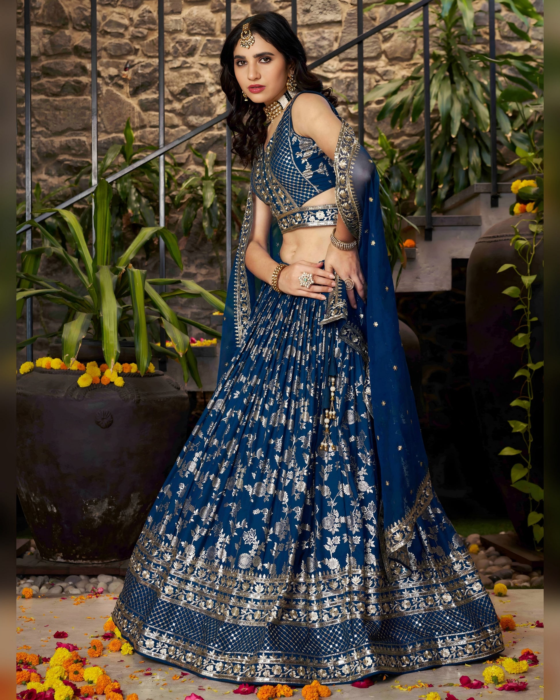Woman in a blue and silver traditional outfit standing outdoors with decorative elements.
