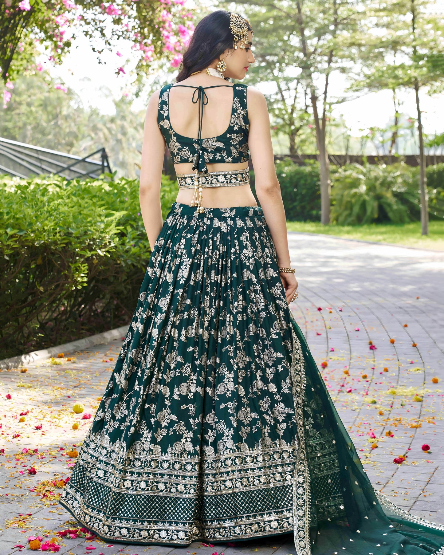 Woman in a green and white embroidered traditional outfit standing outdoors with greenery in the background.