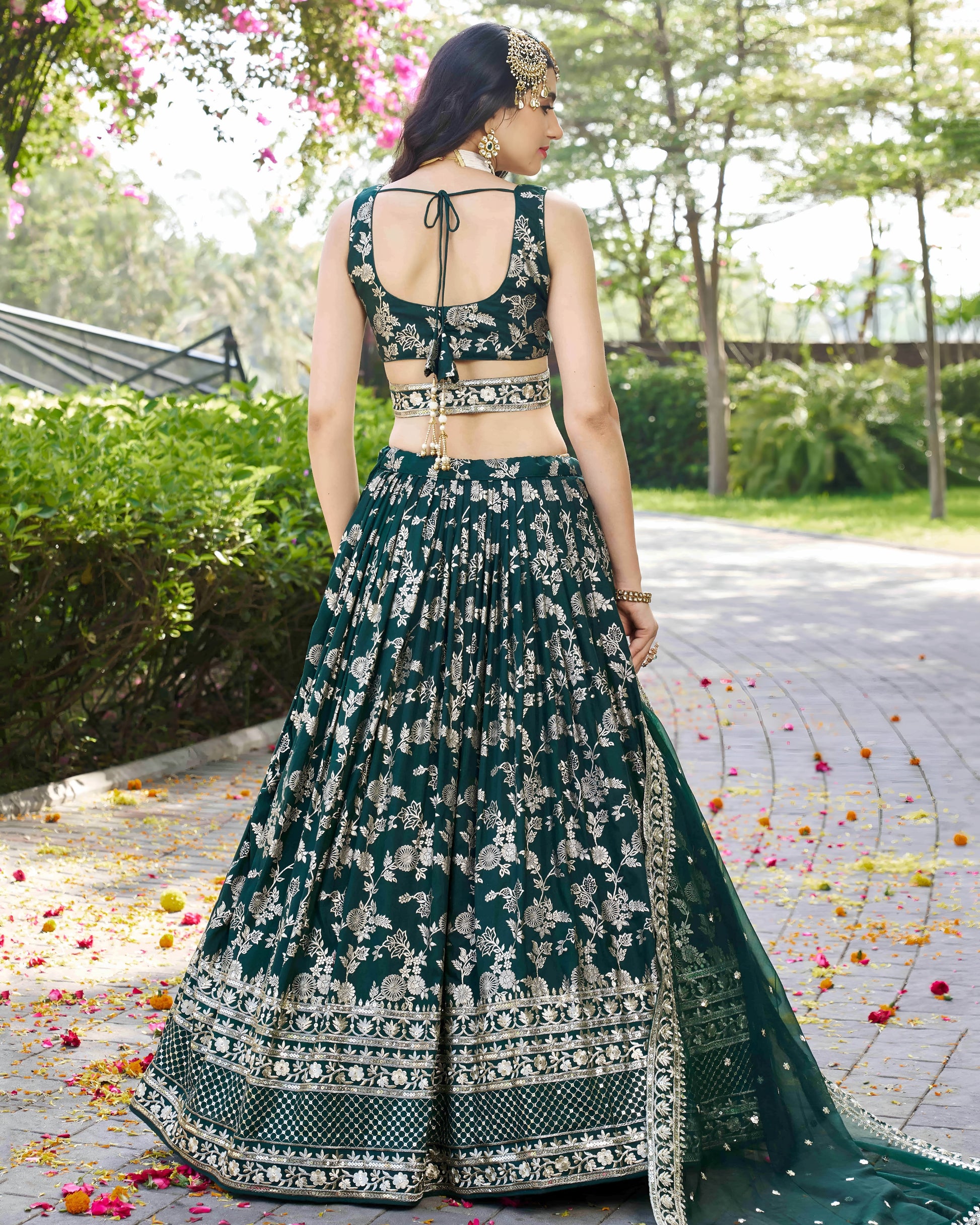 Woman in a green and white embroidered traditional outfit standing outdoors with greenery in the background.