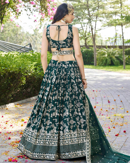 Woman in a green and white embroidered traditional outfit standing outdoors with greenery in the background.