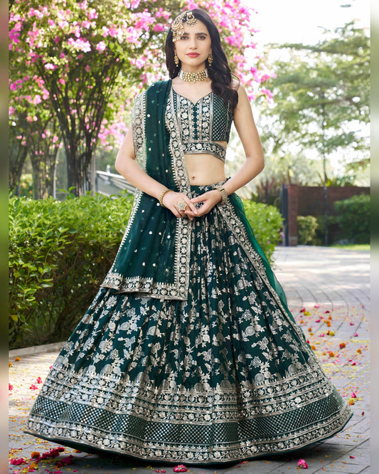 Woman in a green and white traditional outfit standing outdoors with flowers and greenery.