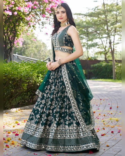 Woman in a green and black embroidered traditional outfit standing outdoors with flowers on the ground.