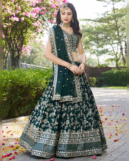 Woman in a dark green embroidered traditional outfit standing outdoors with flowers and greenery.