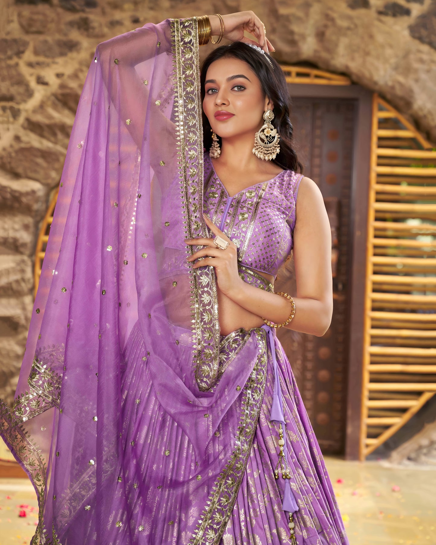 Woman in a purple saree with silver embroidery against a stone wall background