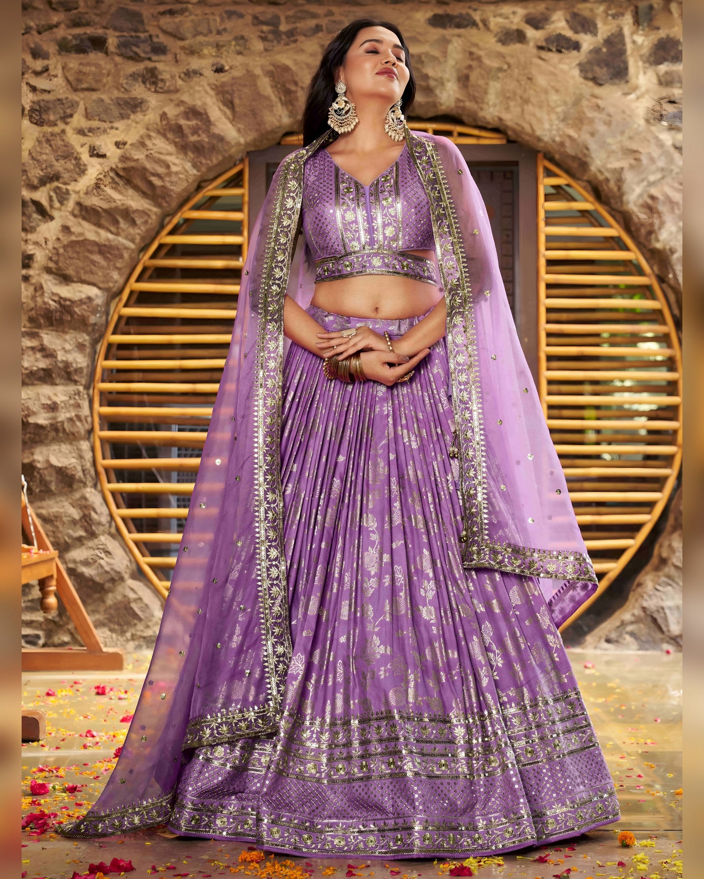 Woman in a purple traditional outfit with silver details against a stone wall.