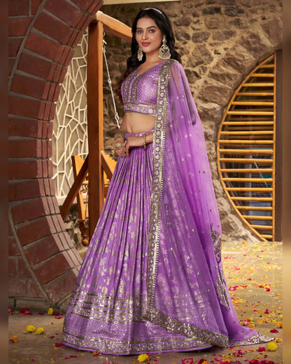 Woman in a purple traditional outfit standing in front of a stone wall.