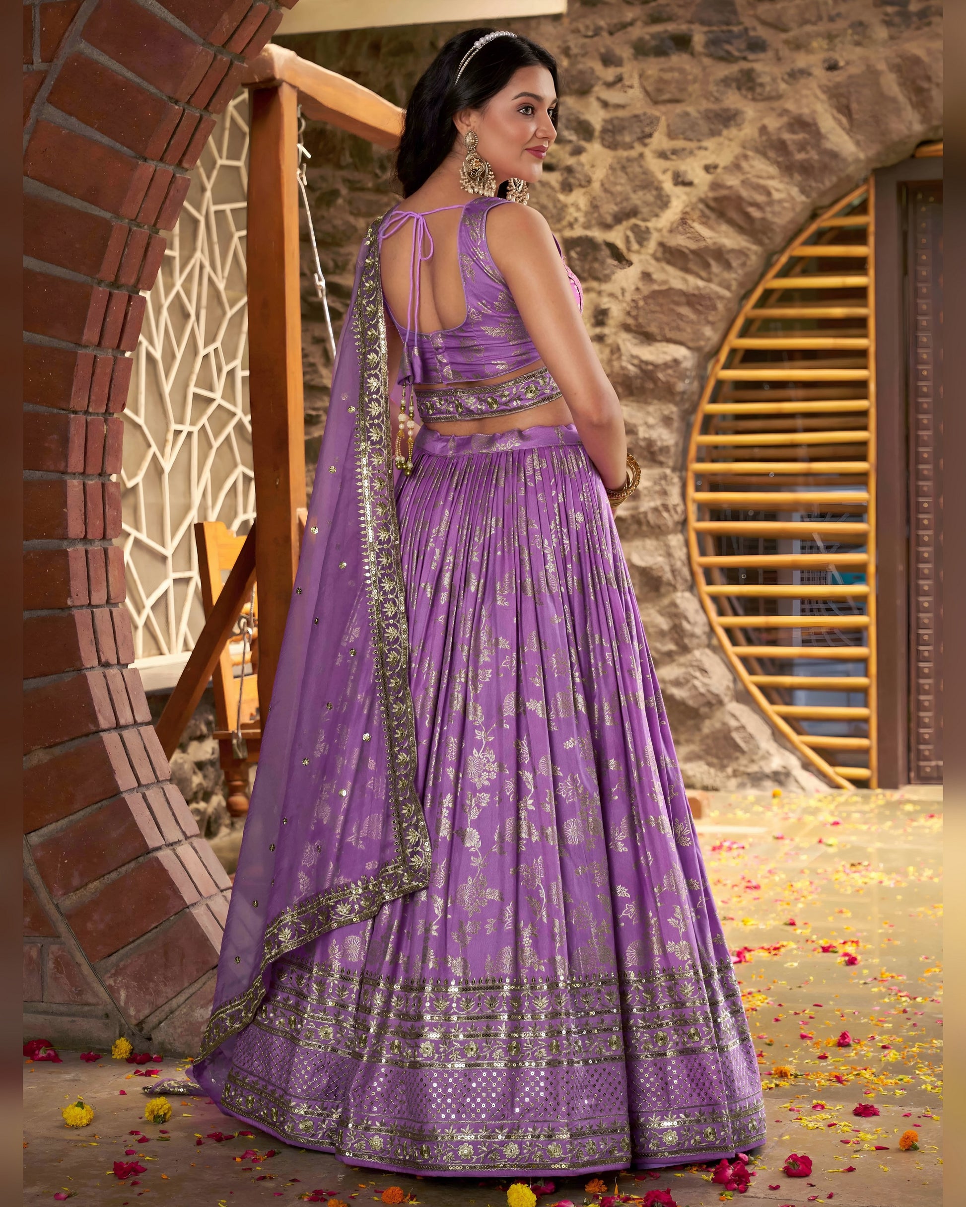 Woman in a purple traditional outfit standing against a stone wall.
