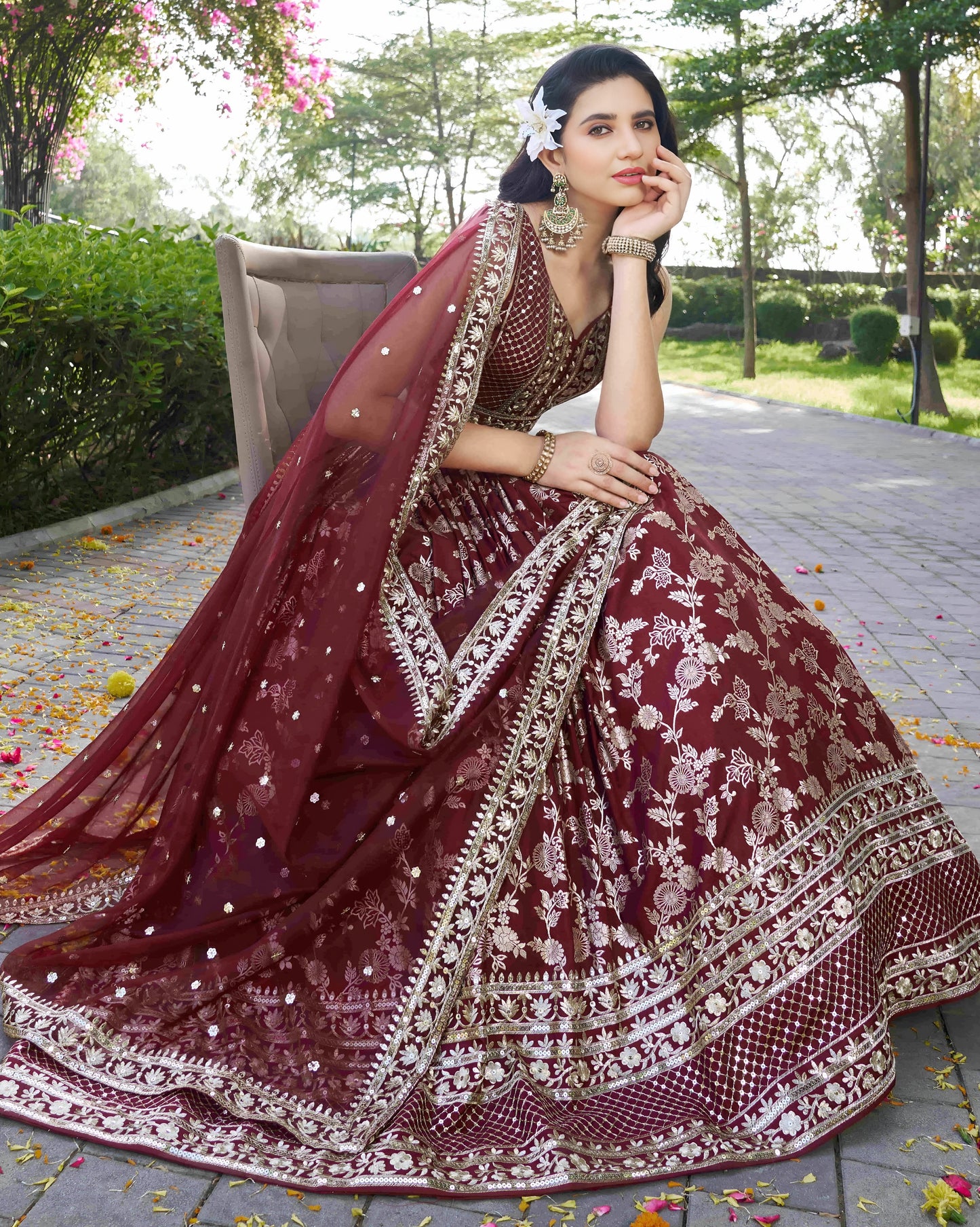 Woman in a traditional maroon and gold embroidered outfit sitting outdoors.