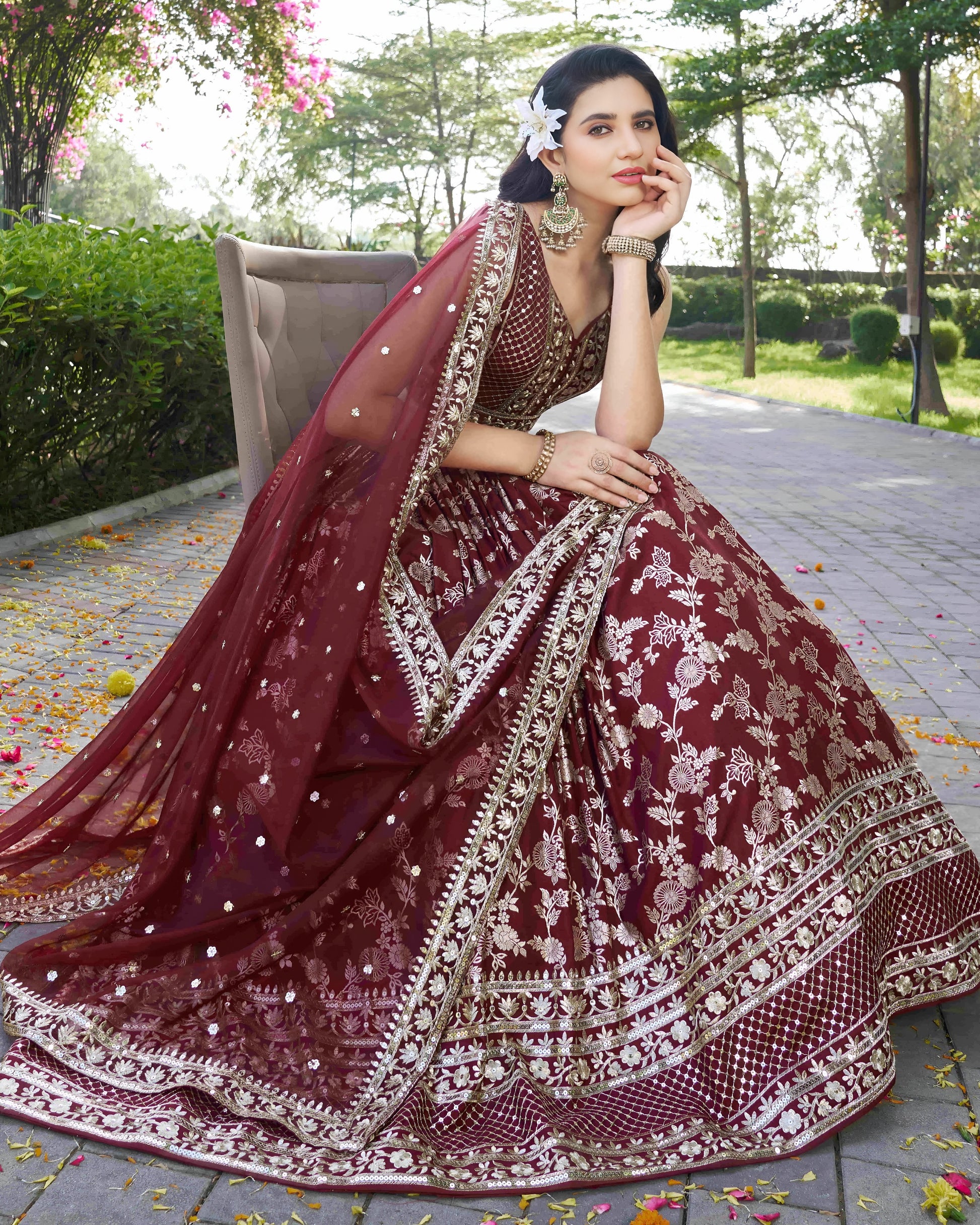 Woman in a traditional maroon and gold embroidered outfit sitting outdoors.