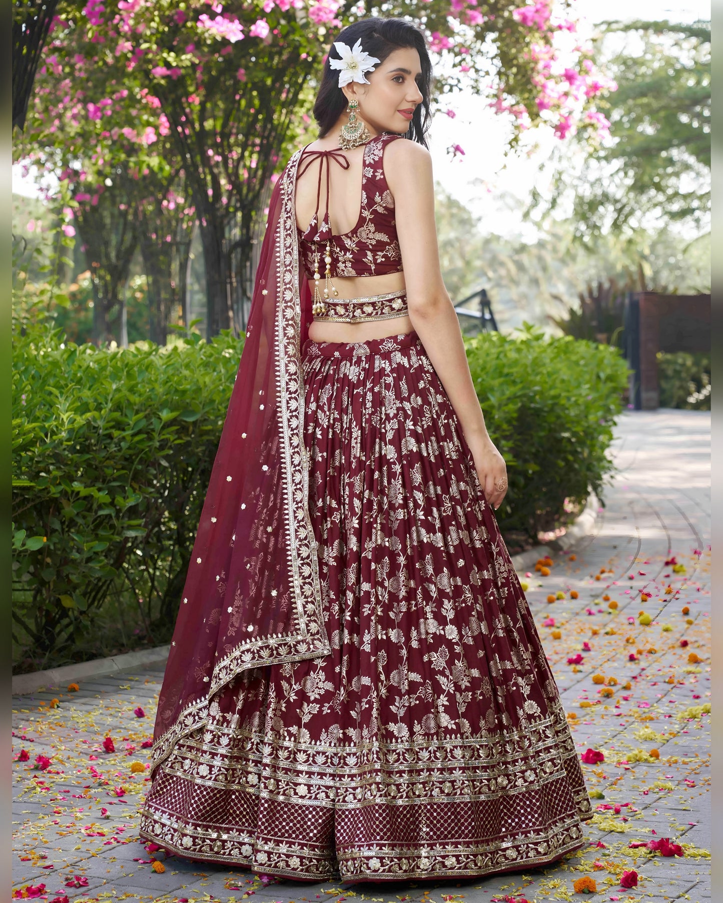 Woman in a maroon traditional outfit with floral decorations in an outdoor setting.