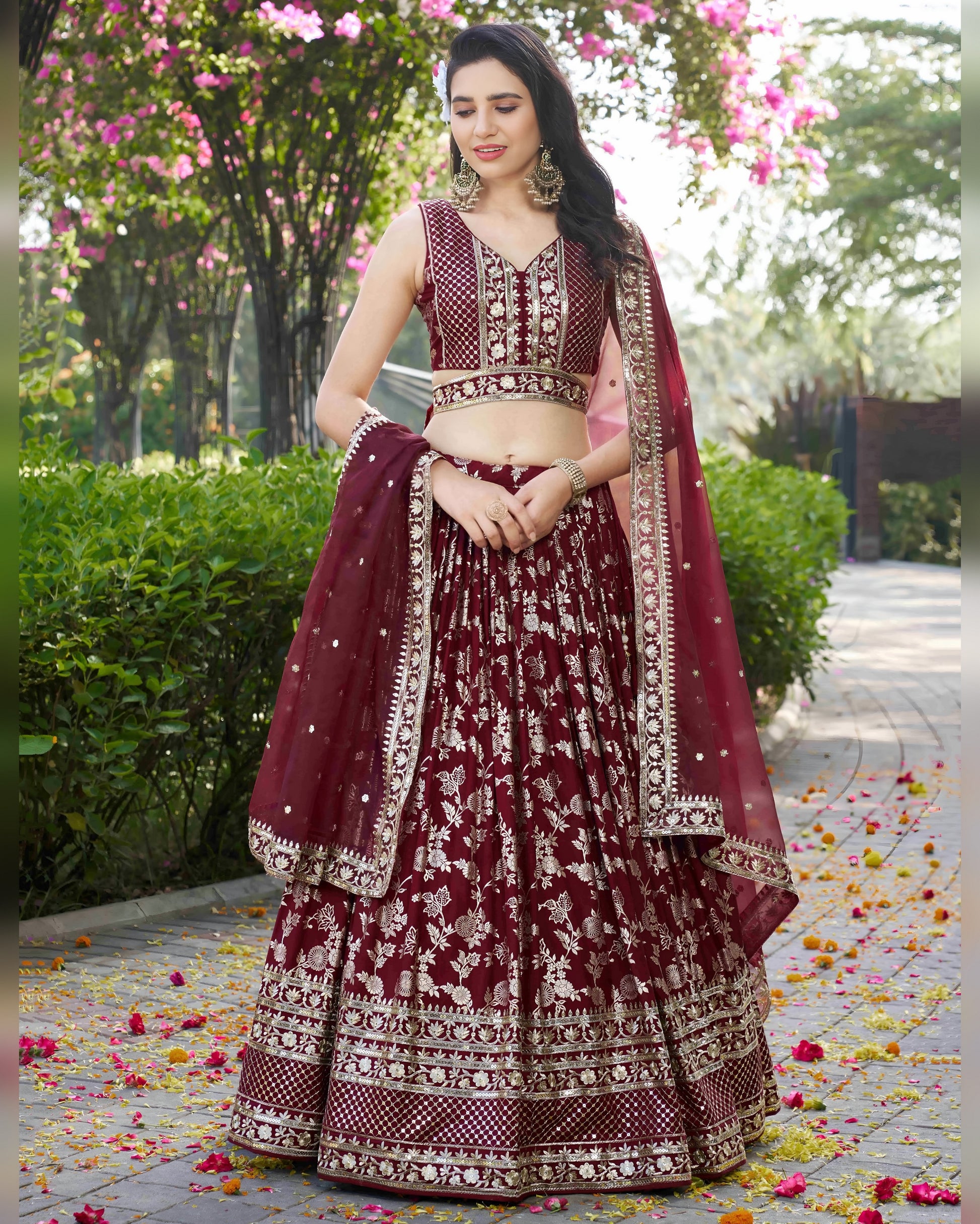 Woman in a maroon traditional outfit with floral patterns standing outdoors.