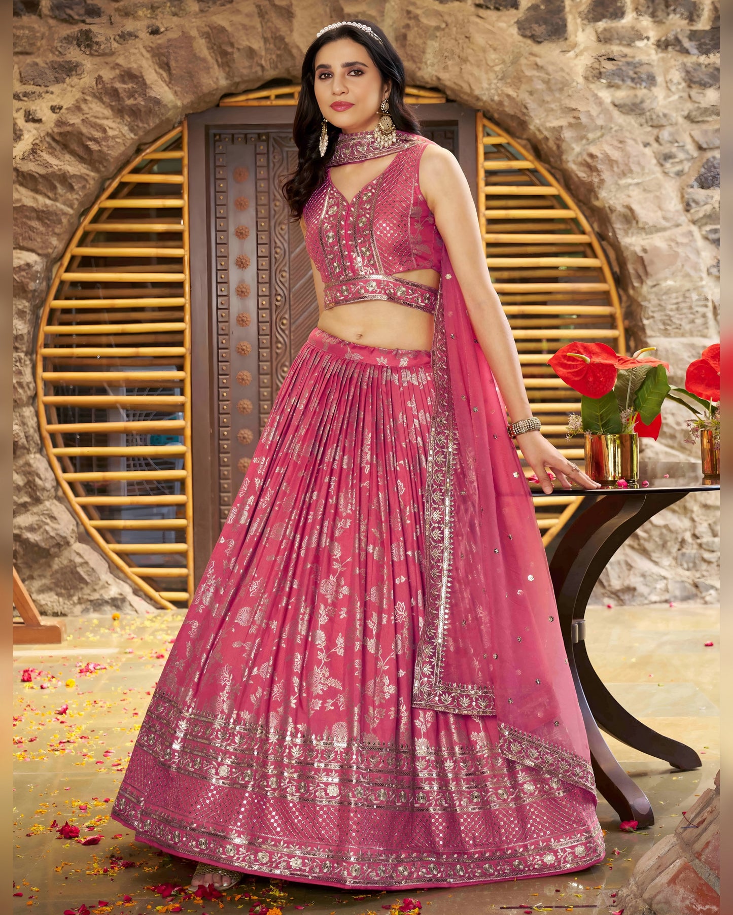 Woman in a pink traditional outfit with a stone wall and decorative elements in the background