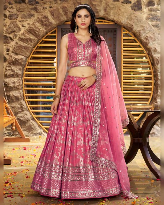 Woman in a pink traditional outfit with intricate designs against a stone wall background