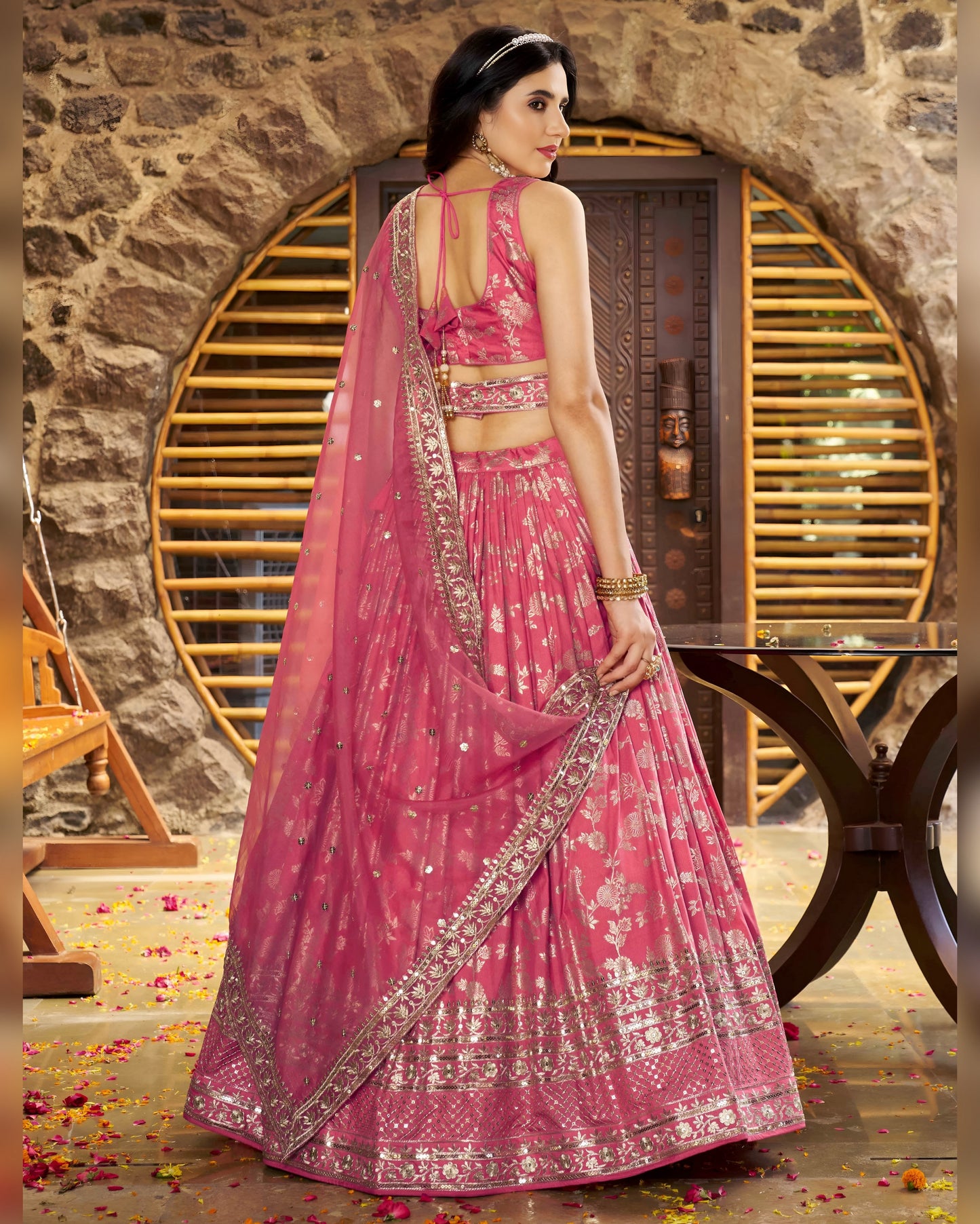 Woman in a pink traditional outfit with intricate designs against a stone wall.