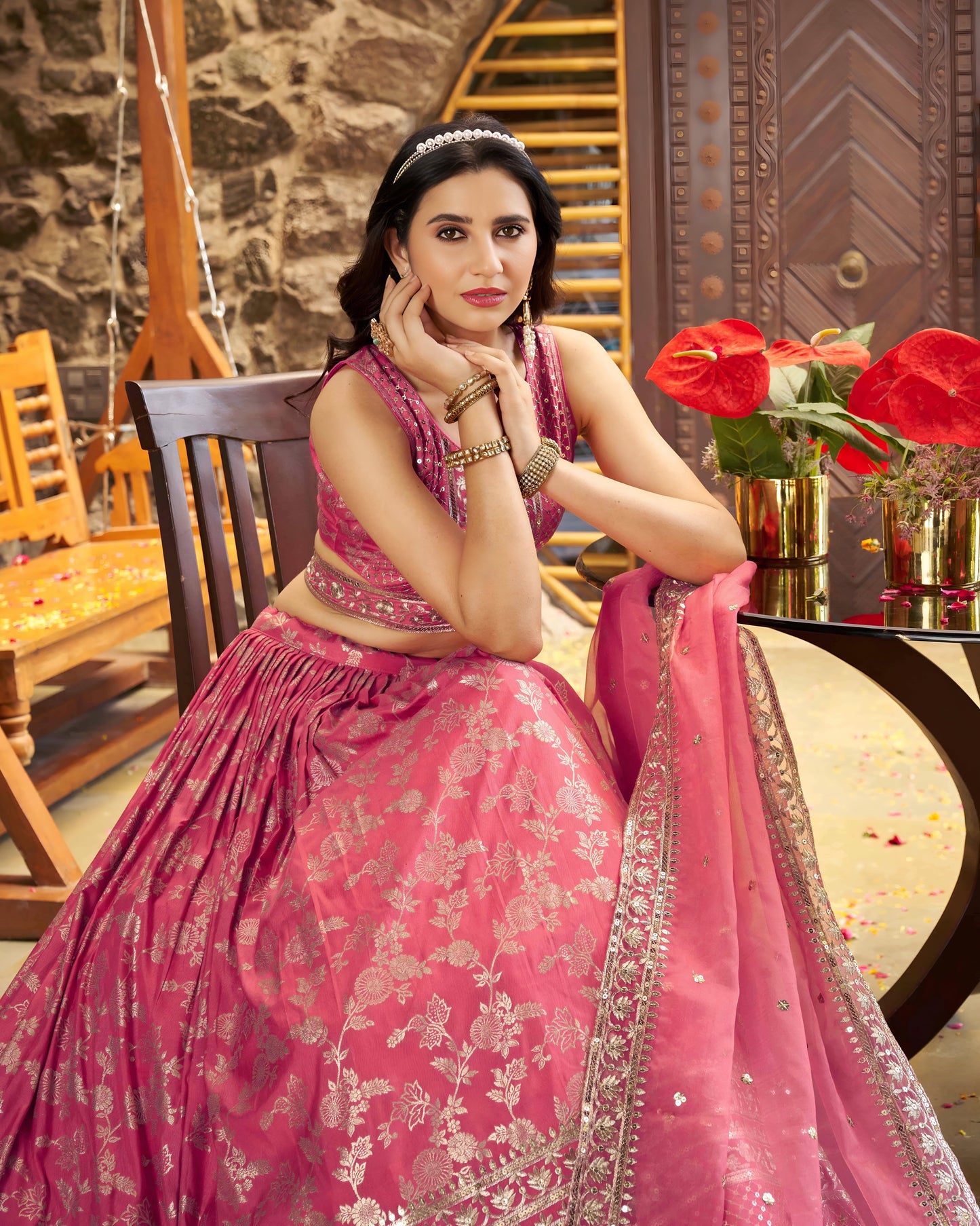 Woman in a pink traditional outfit sitting indoors with decorative elements.