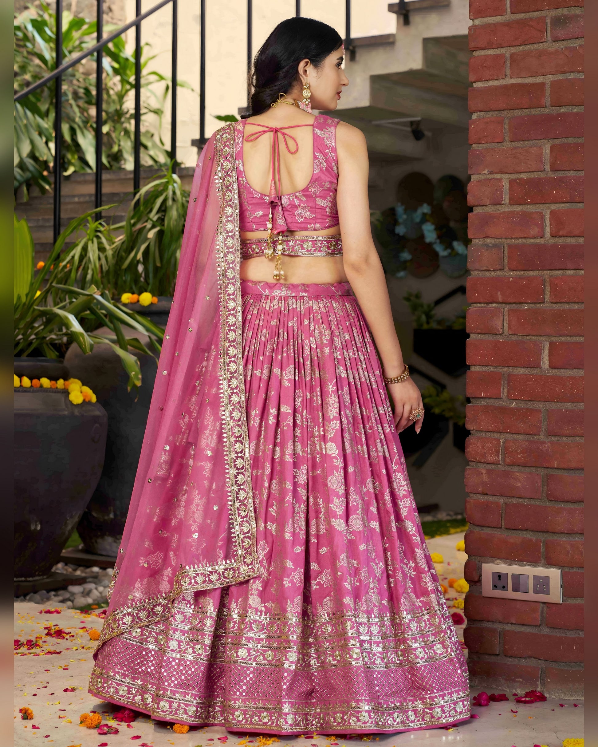 Woman in a pink traditional outfit standing outdoors near a staircase.