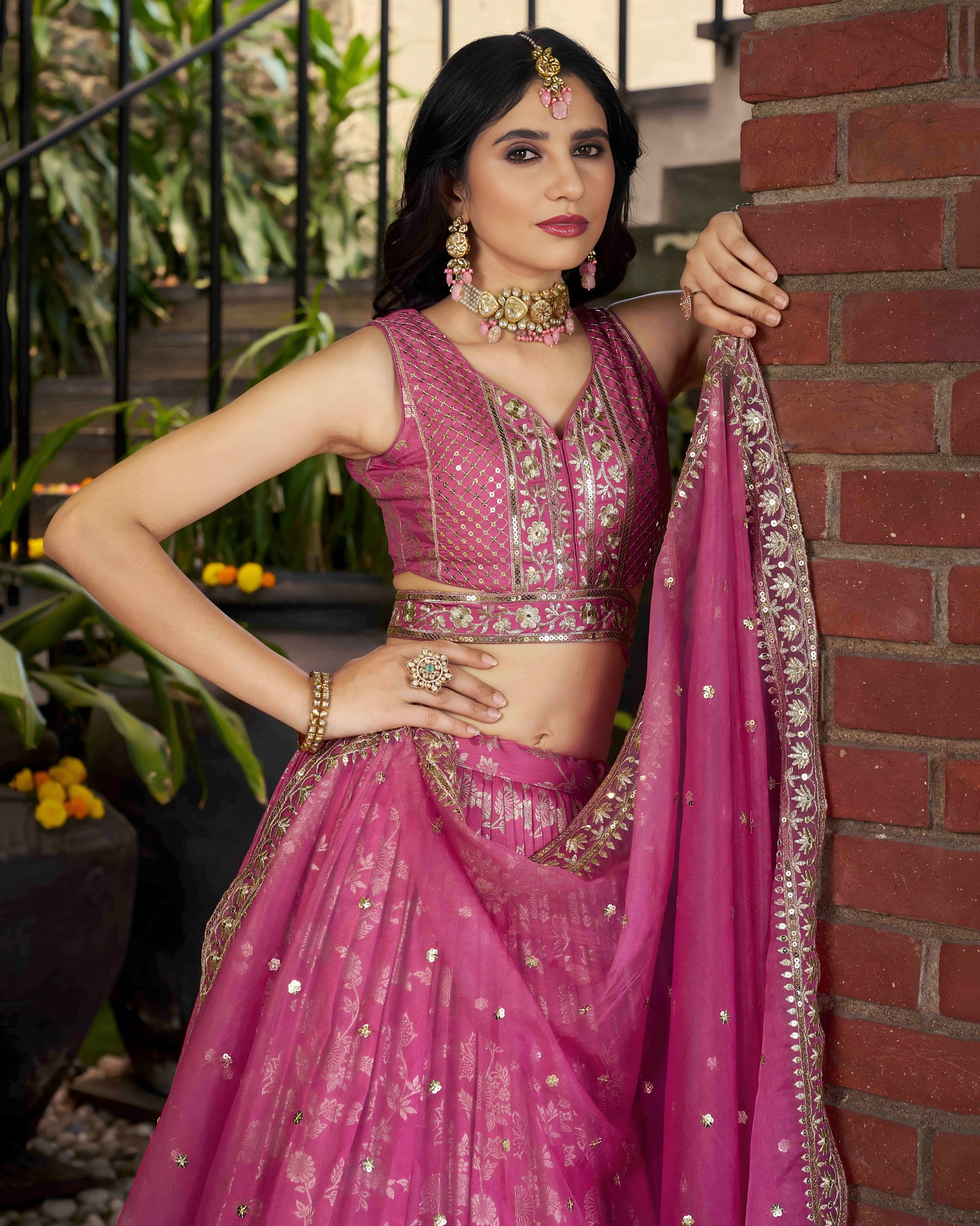 Woman in a pink traditional outfit standing against a brick wall.